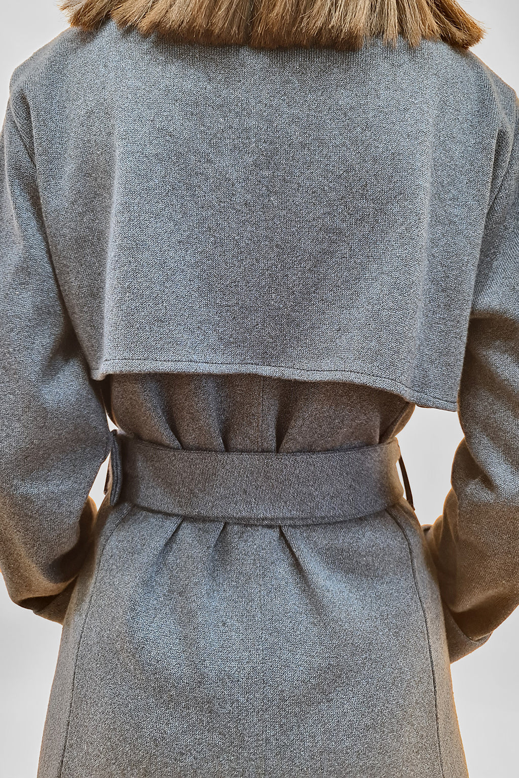 Back view of a person wearing a stylish gray wool coat with a belt and a wide collar