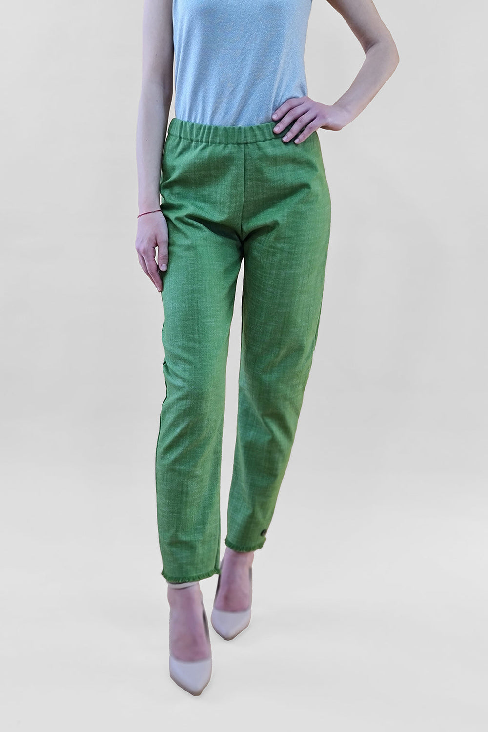 Woman wearing green pants and a grey top with white high heels