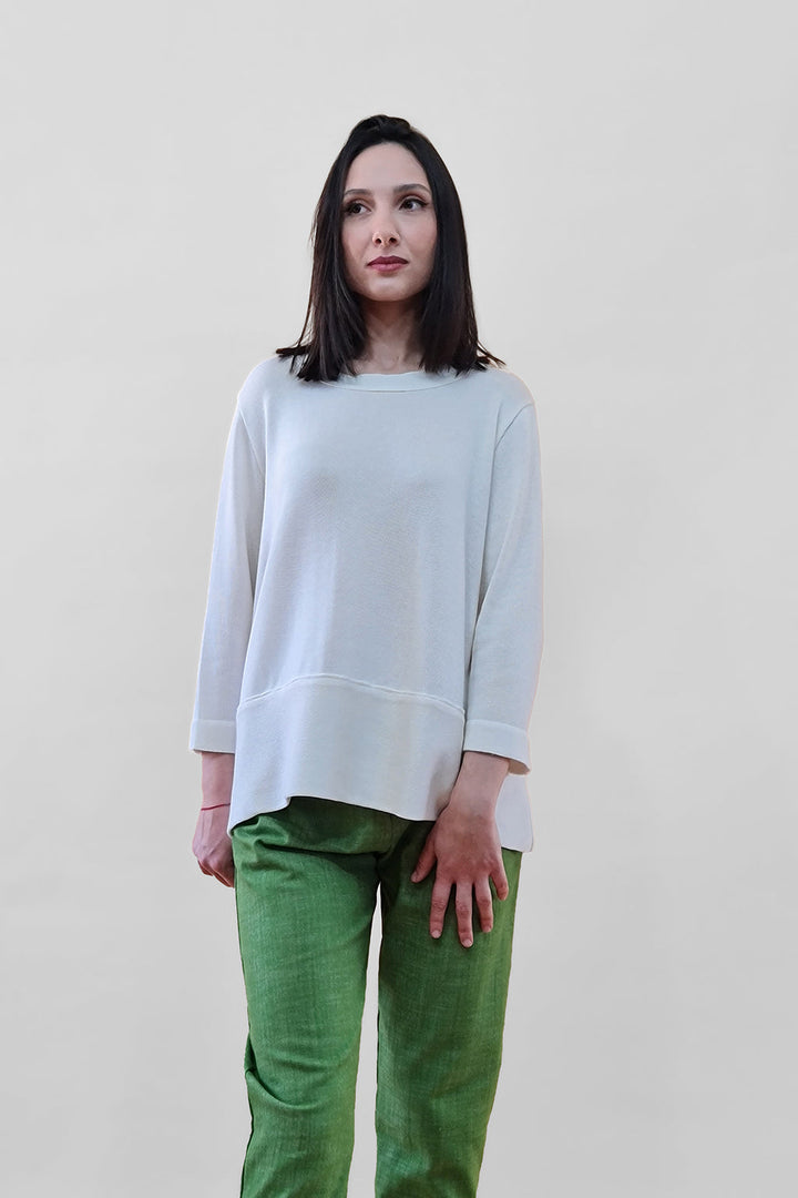 Woman wearing a white top and green pants against a plain background
