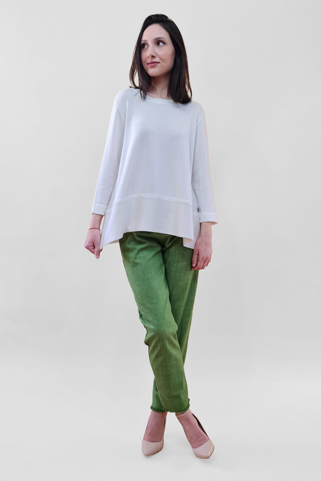 Woman in white sweater and green pants posing against a plain background