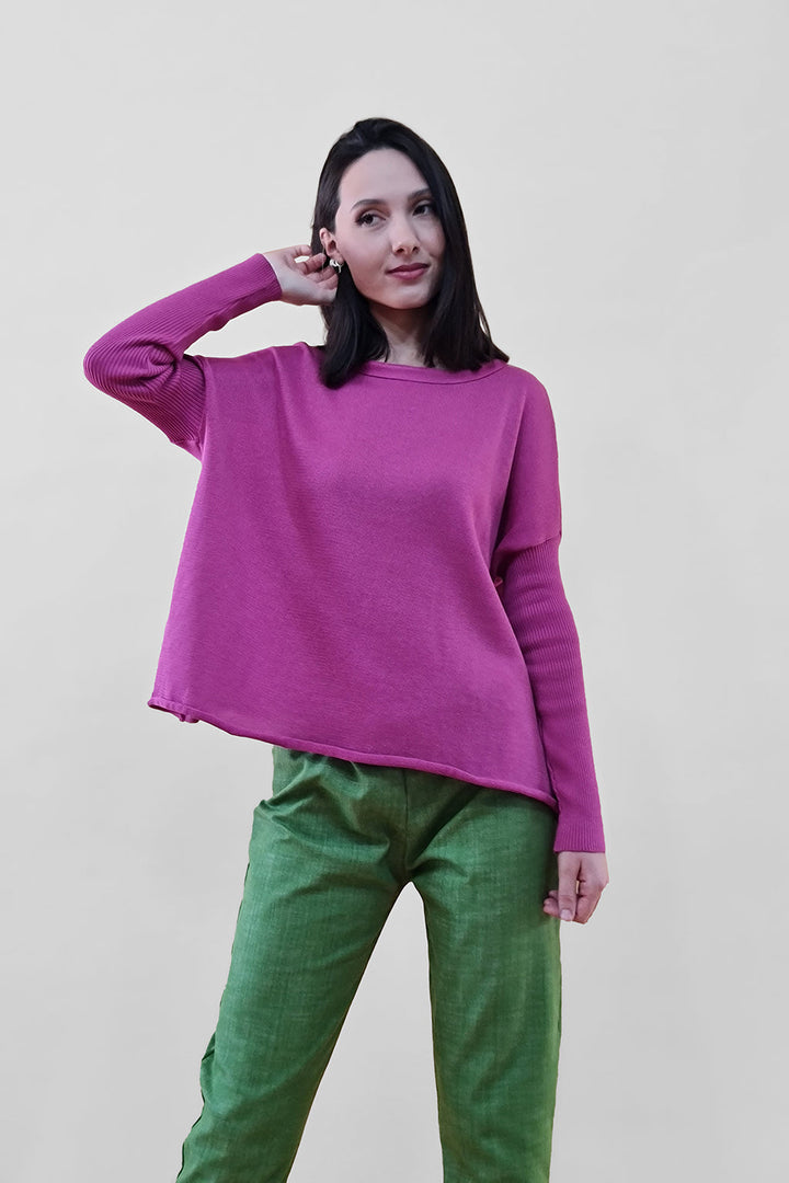 Woman wearing a pink sweater and green pants, posing against a white background