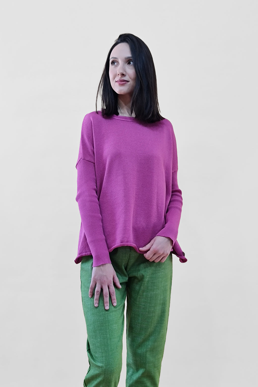 Woman wearing pink sweater and green pants against a plain background