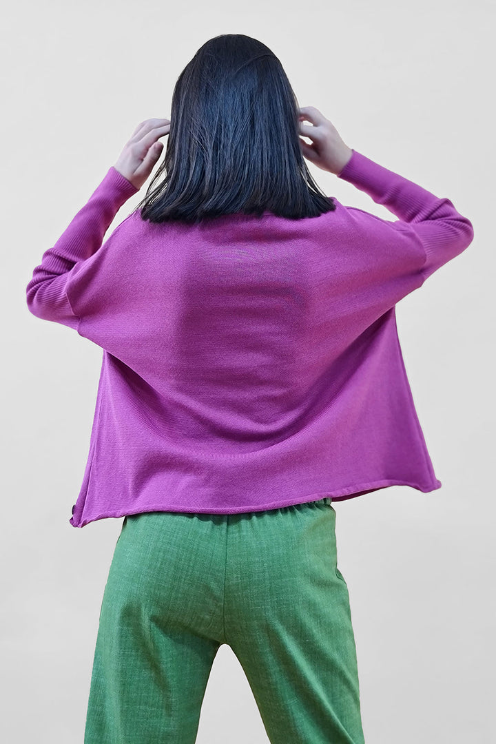 Rear view of person wearing a purple top and green pants adjusting hair