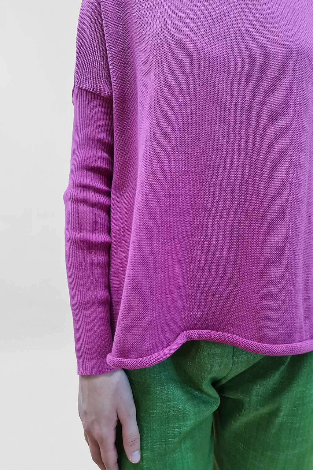 Person wearing a pink sweater and green pants on a white background