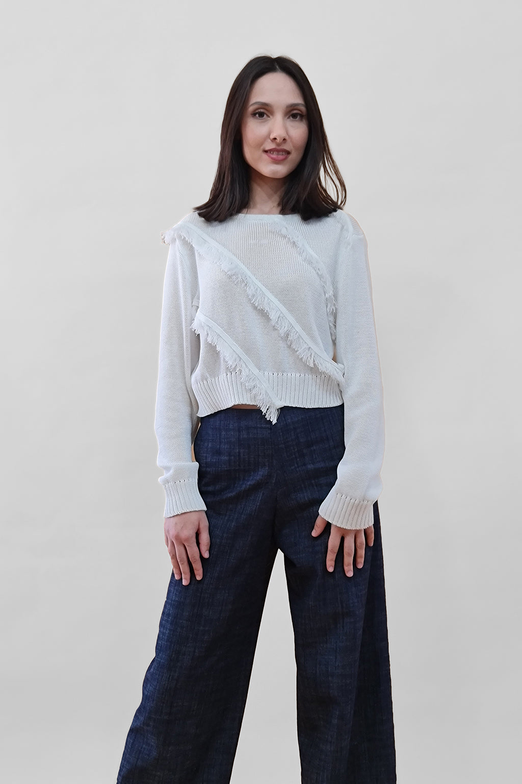 Woman in stylish white sweater and dark wide-leg pants against a plain background