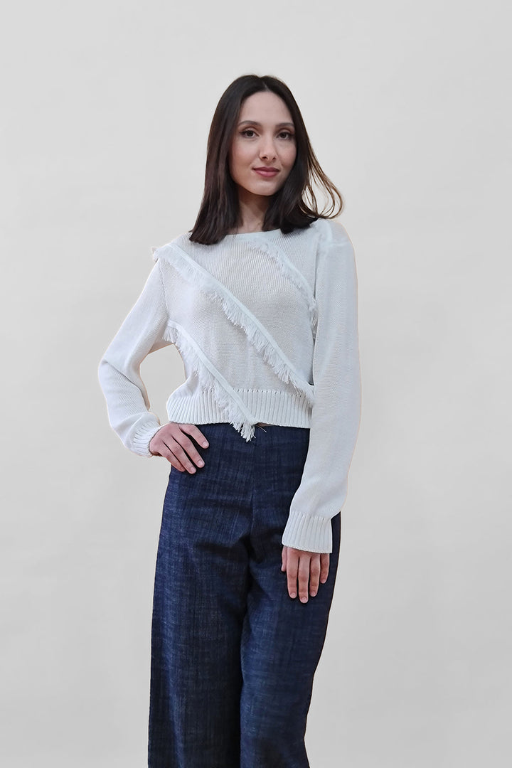 Woman wearing white sweater and dark jeans standing against plain background