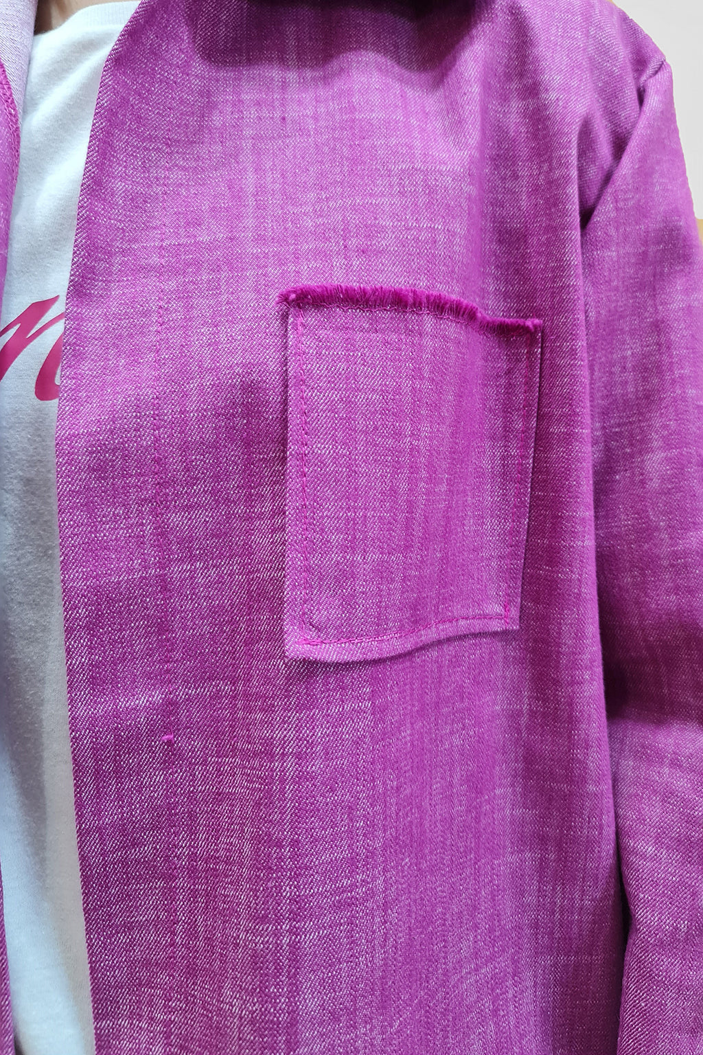 Close-up of a person wearing a pink textured jacket with a square chest pocket over a white shirt