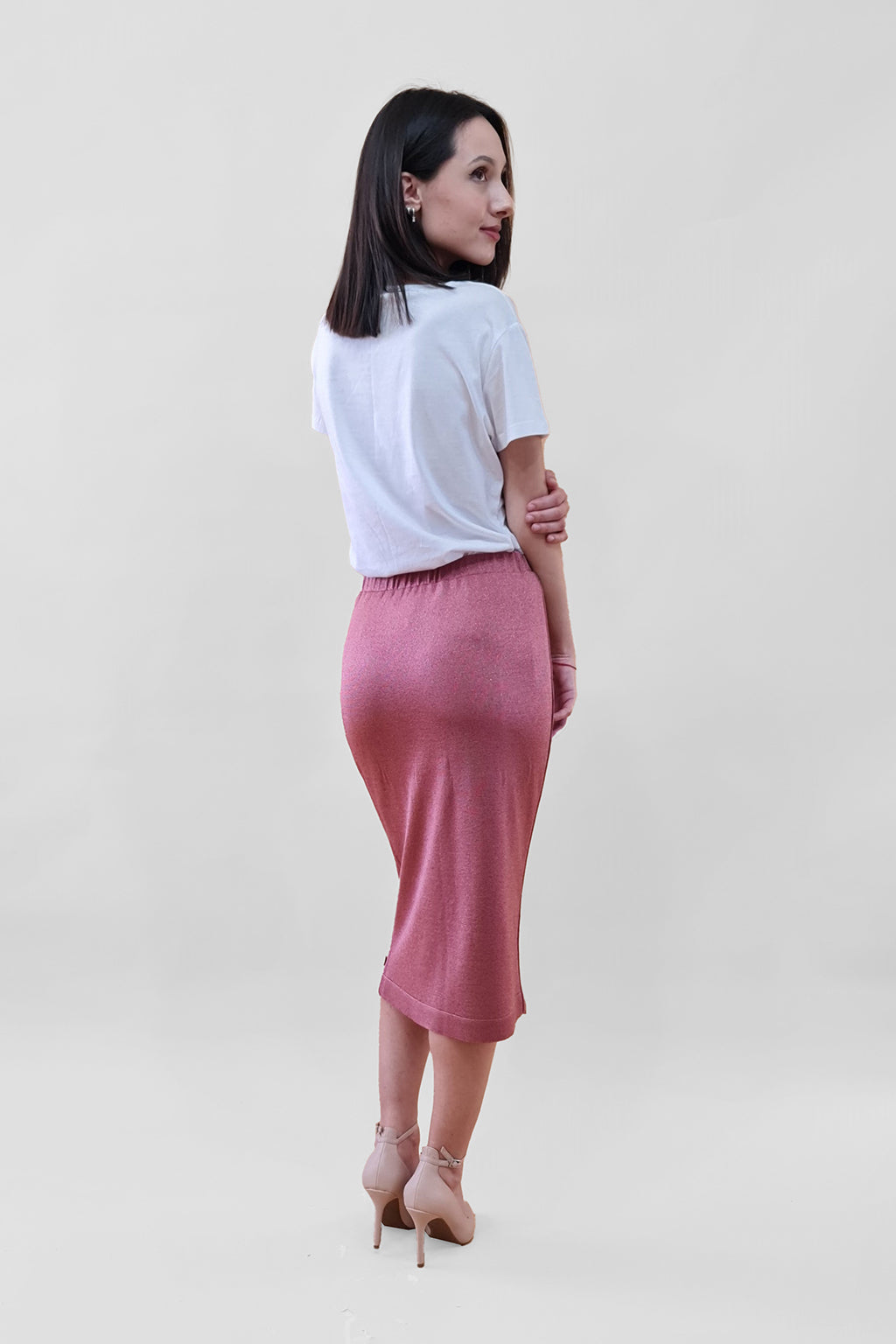 Woman wearing a white top and pink skirt with heels, facing away