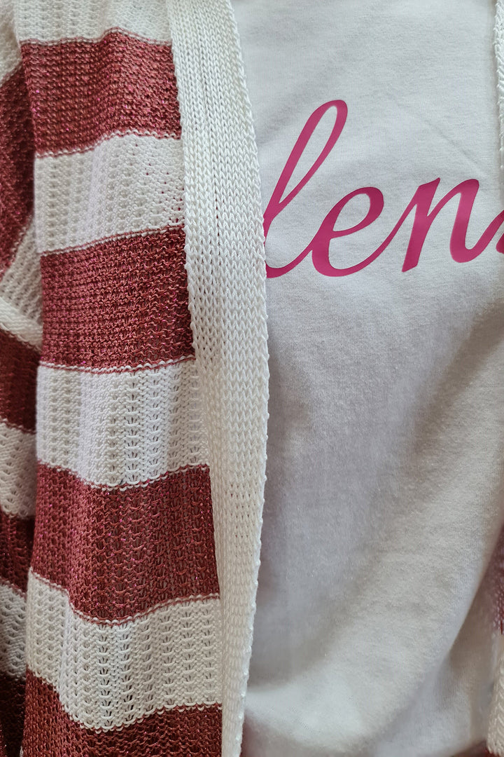 Close-up of a white and pink striped knit cardigan over a white shirt with pink text