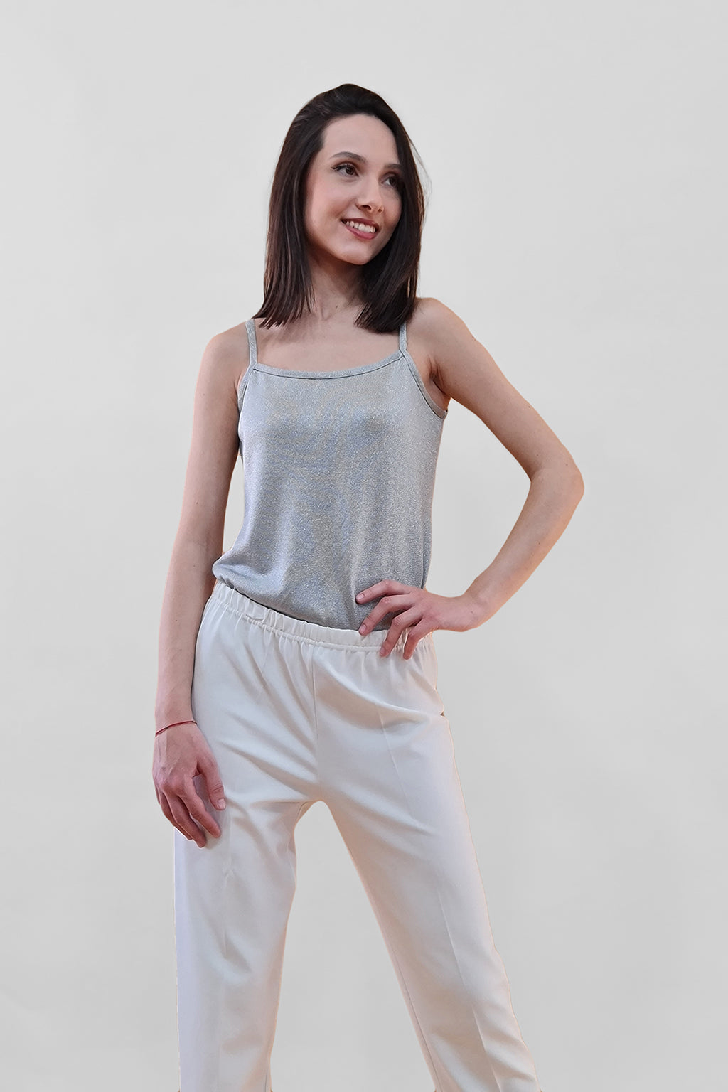 Woman models gray tank top and white high-waisted pants against light background