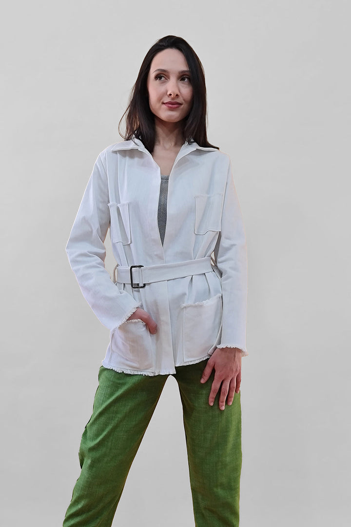 Woman wearing white belted jacket and green pants against a plain background