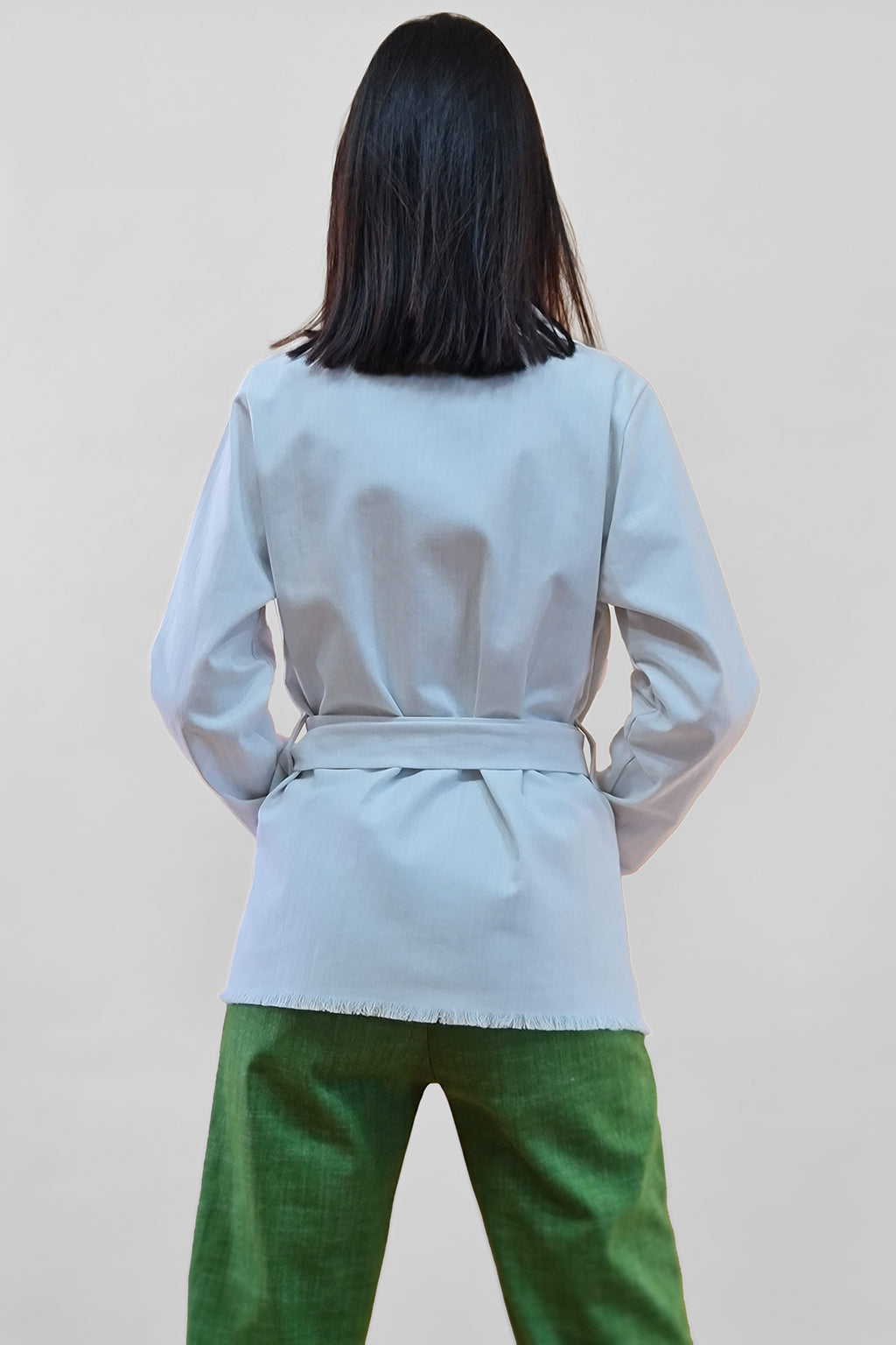 Back view of woman in gray blazer and green pants against white background