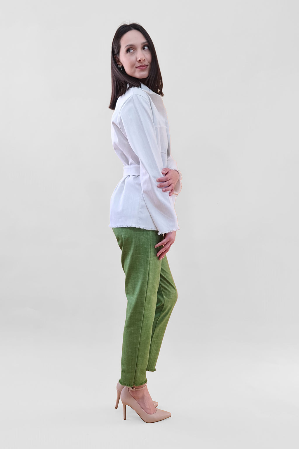 Woman in a white blouse and green pants standing on a white background