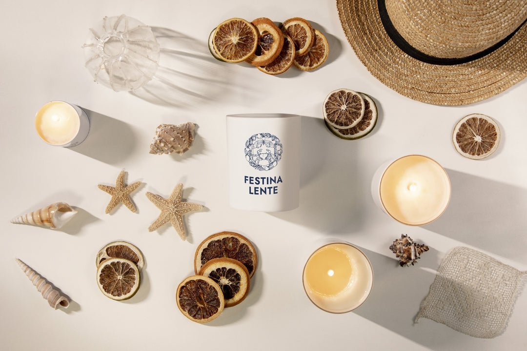 Overhead view of a candle, seashells, dried citrus slices, starfish, and a straw hat arranged on a white surface