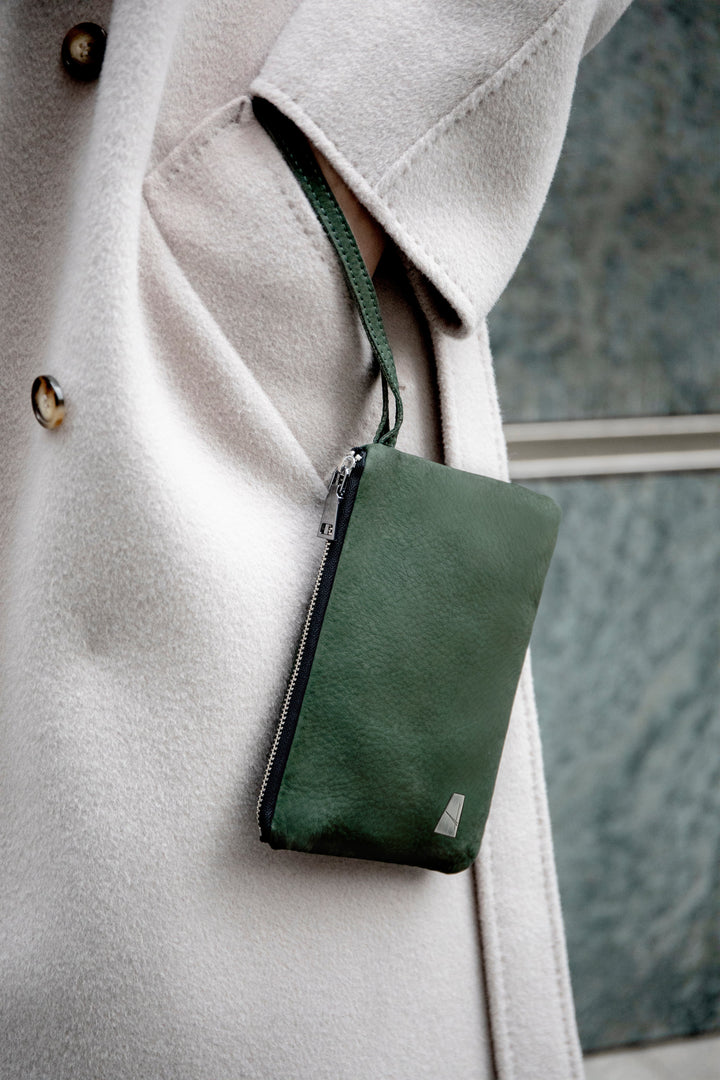Person wearing a beige coat with a green wristlet bag attached to the pocket