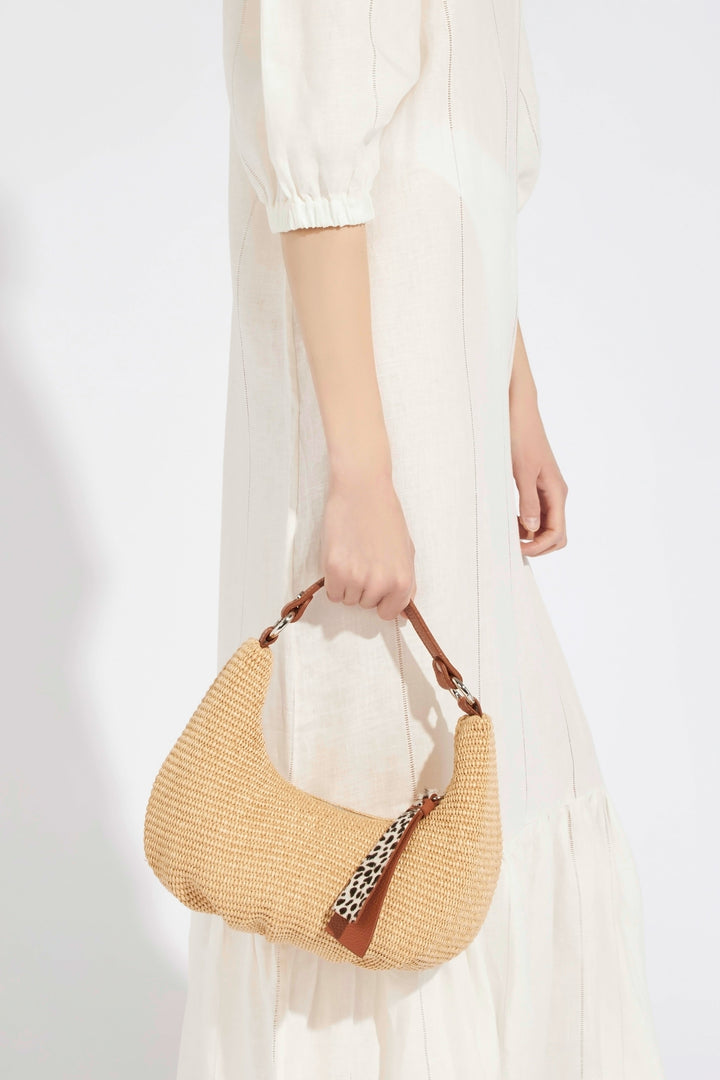 Person in white dress holding a stylish woven handbag with a leopard print accessory