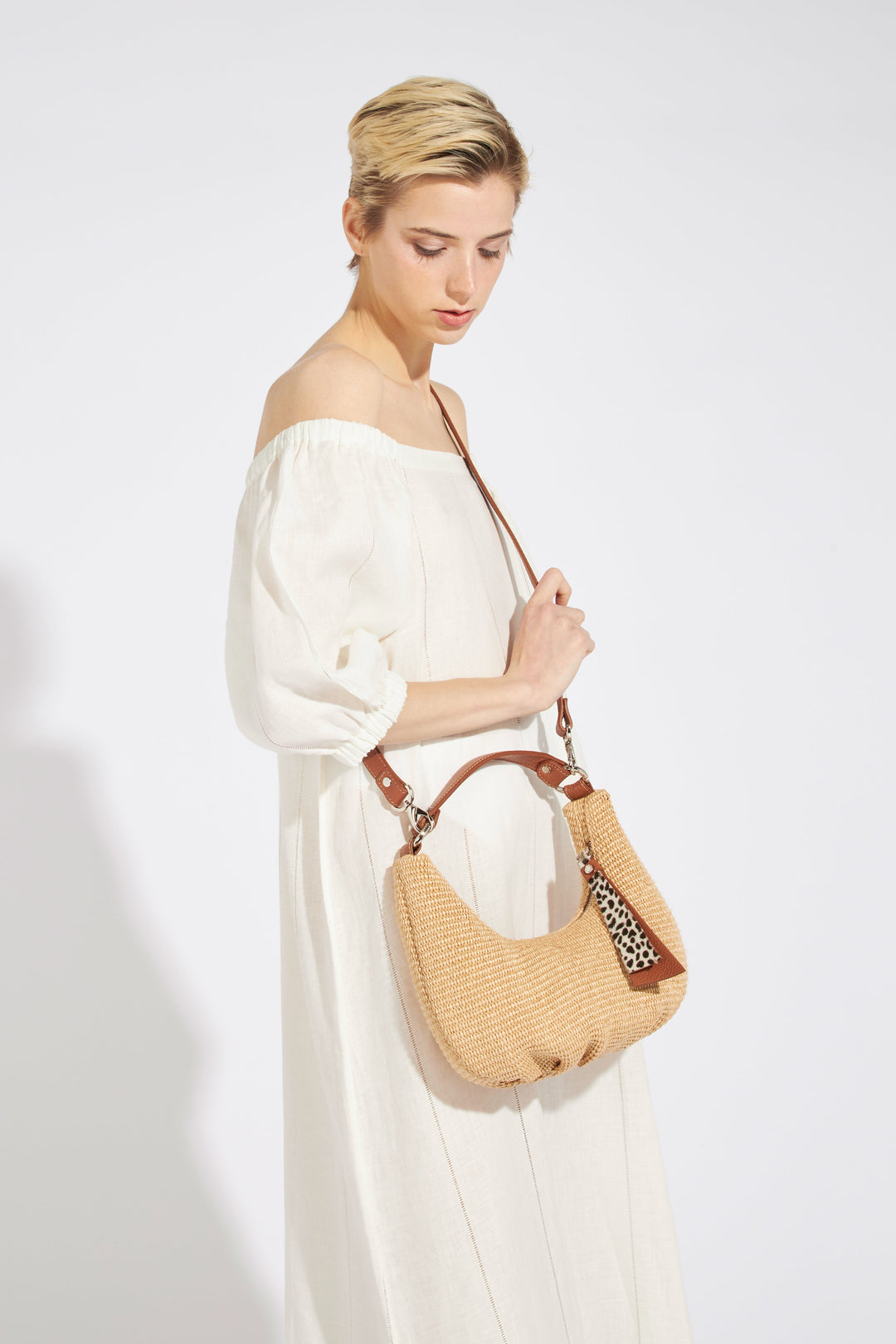 Woman in white off-shoulder dress holding woven handbag with leopard print keychain