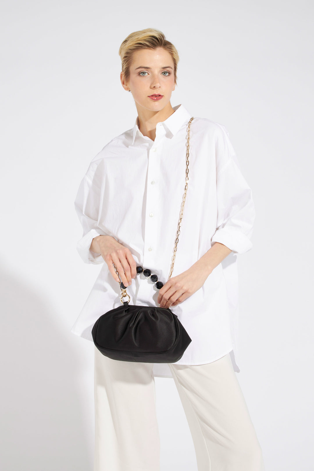 Woman wearing a white oversized shirt and holding a stylish black handbag