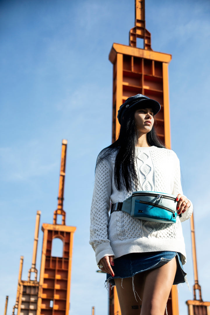 Woman in white sweater and cap standing in front of industrial structures under a blue sky