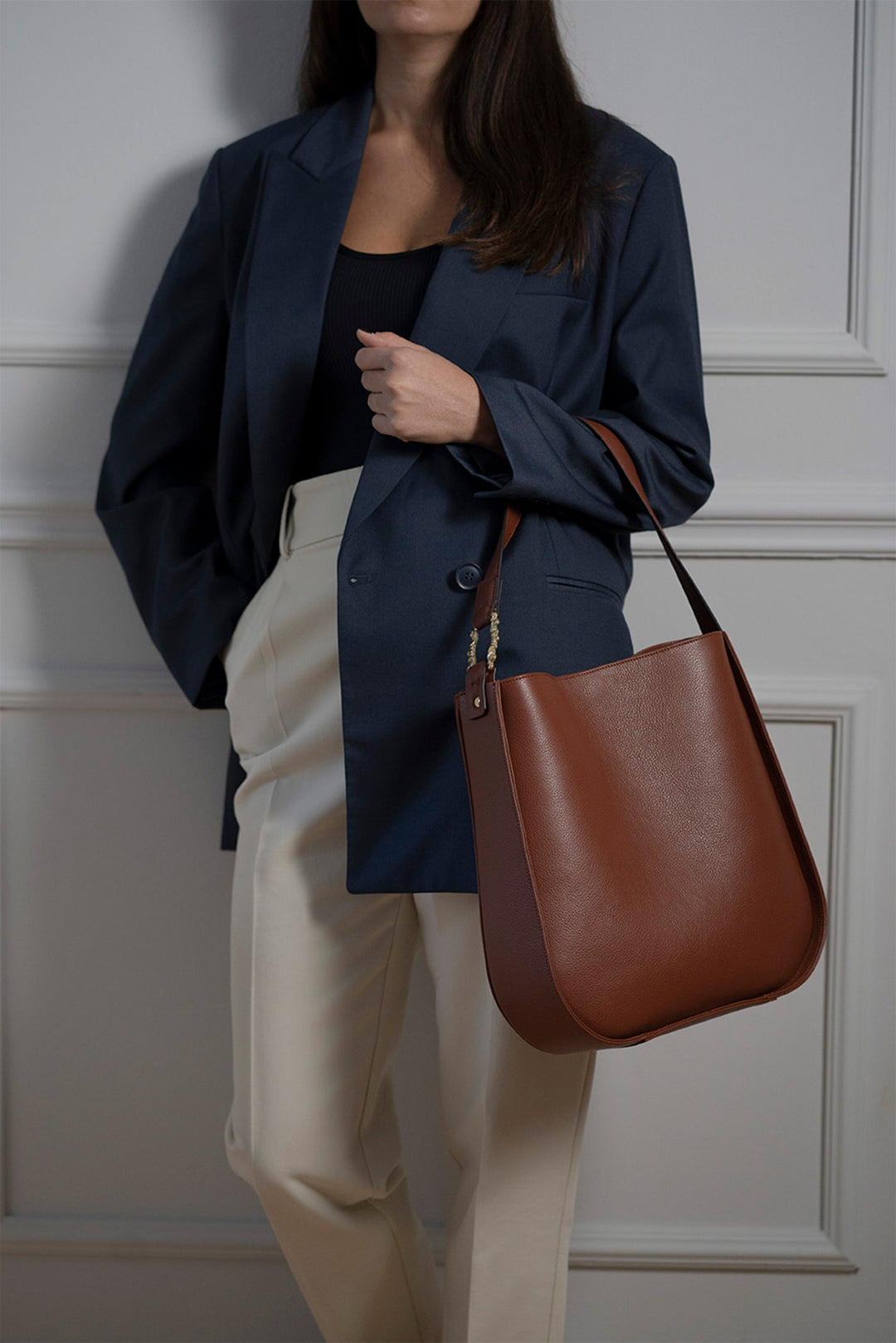 Woman in a navy blazer and white pants holding a brown leather handbag