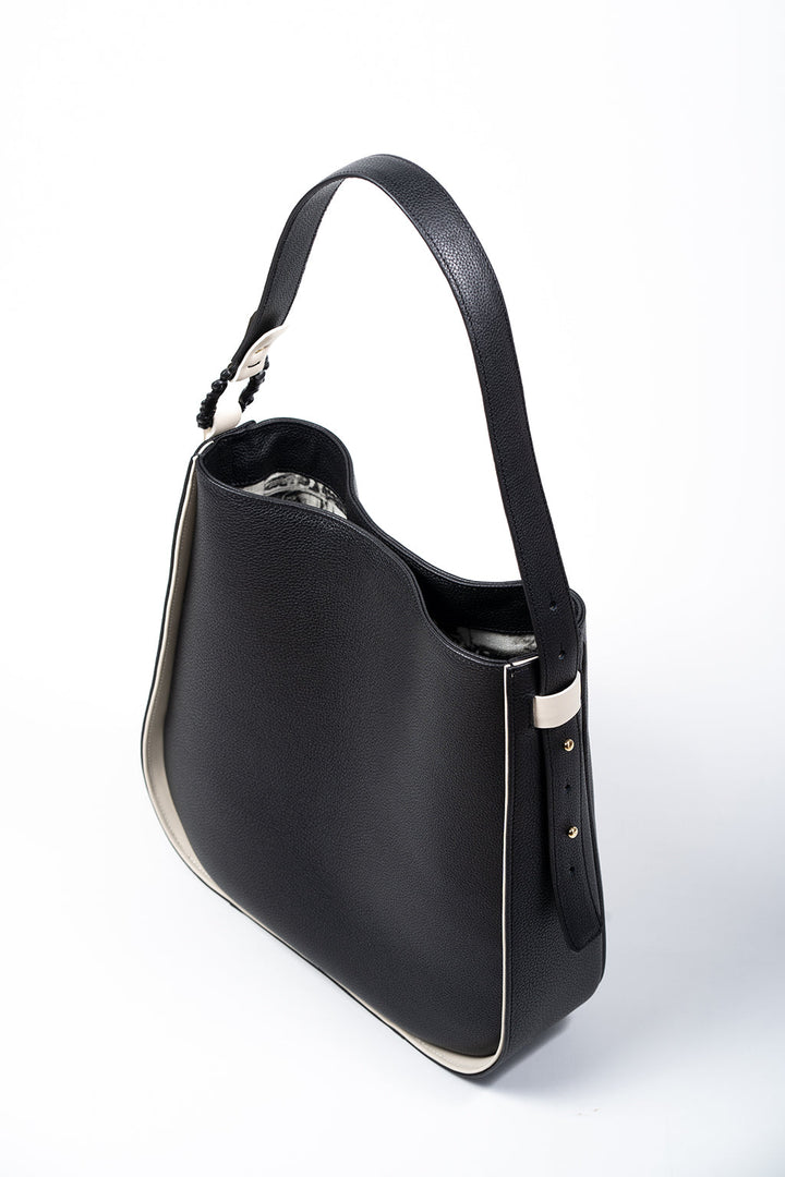 Black leather handbag with white trim and shoulder strap on white background