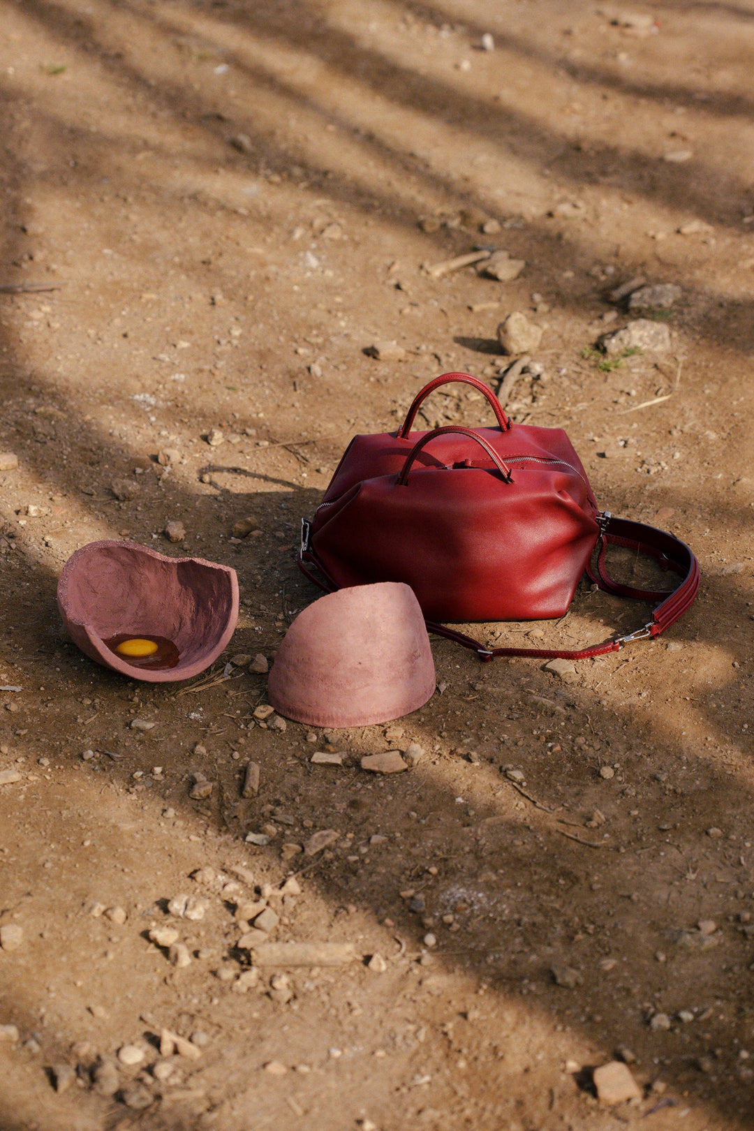 Red handbag on brown dirt ground with broken clay pot containing egg yolk