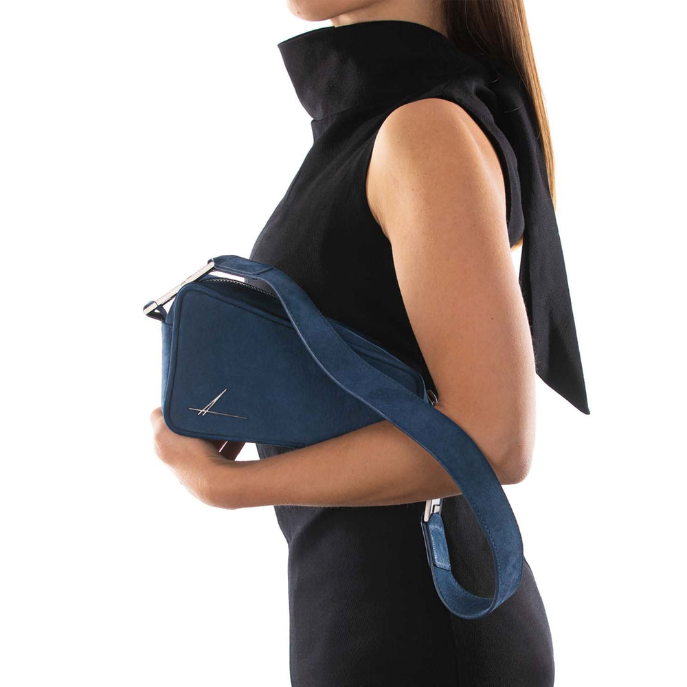 Woman holding a stylish navy blue leather handbag in a sleek black dress against a white background