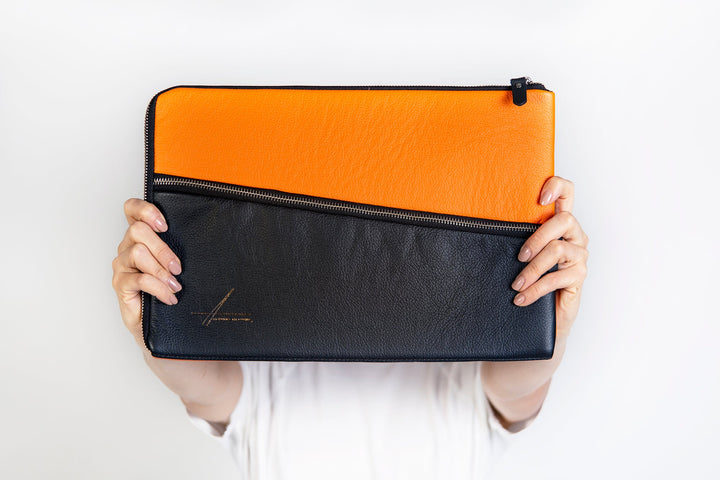 Person holding an orange and black leather clutch against a white background