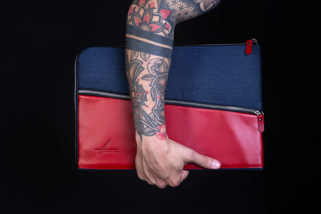 Person with tattooed arm holding stylish red and blue laptop sleeve