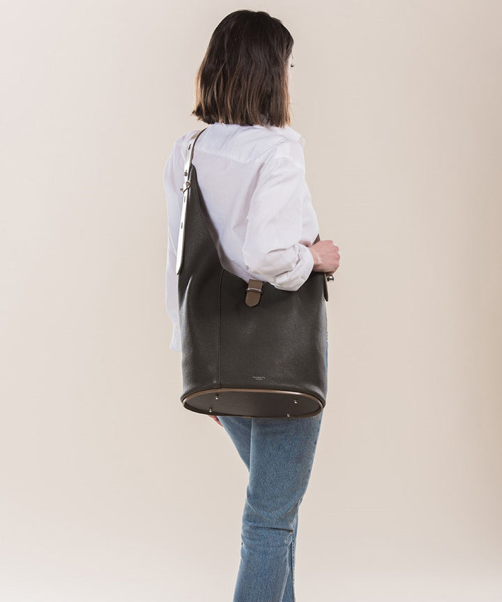 Woman wearing a white blouse and blue jeans carrying a large black leather handbag over her shoulder