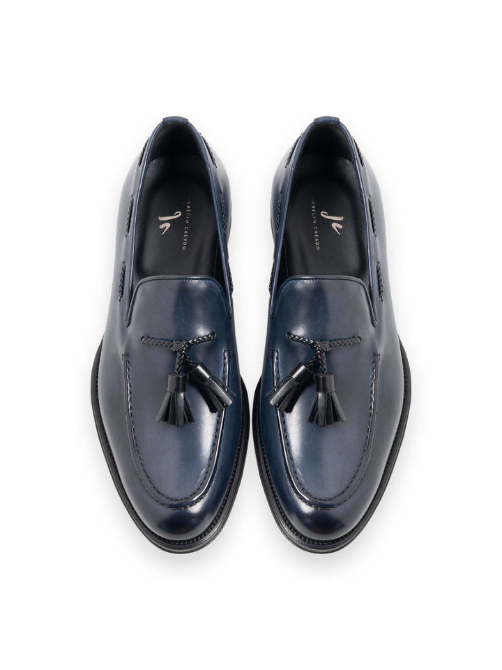 Top view of elegant navy leather loafers with tassel details on a white background