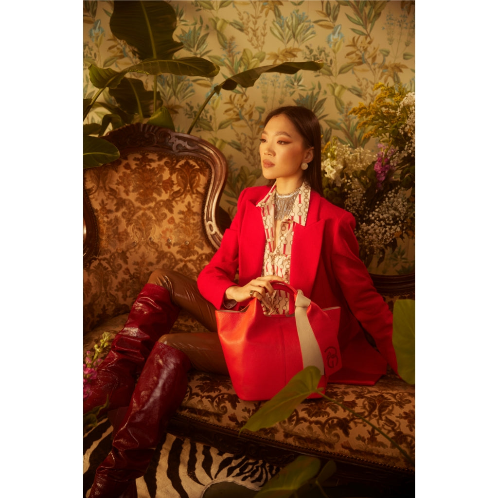 Woman in red blazer with handbag seated on ornate sofa in lush, tropical setting