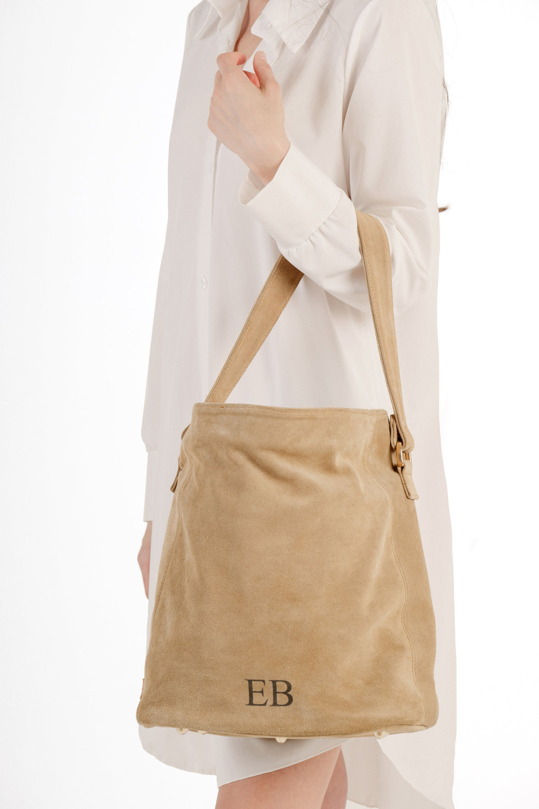 Woman holding beige suede handbag with initials EB