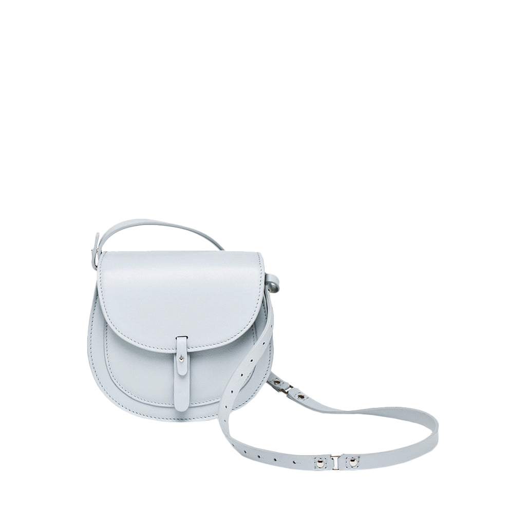 Light gray crossbody bag with adjustable strap and flap closure against a white background
