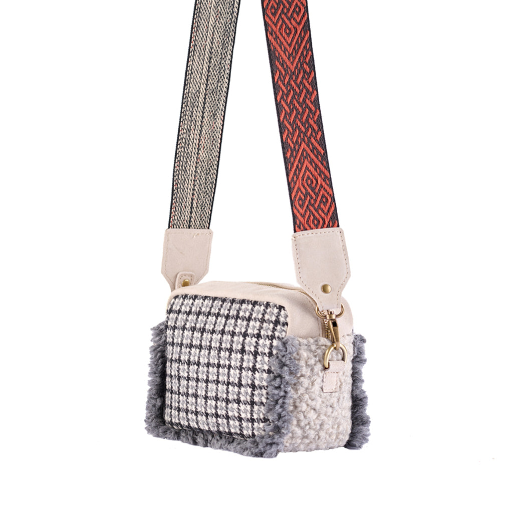 Stylish houndstooth pattern crossbody bag with decorative strap hanging, isolated on white background