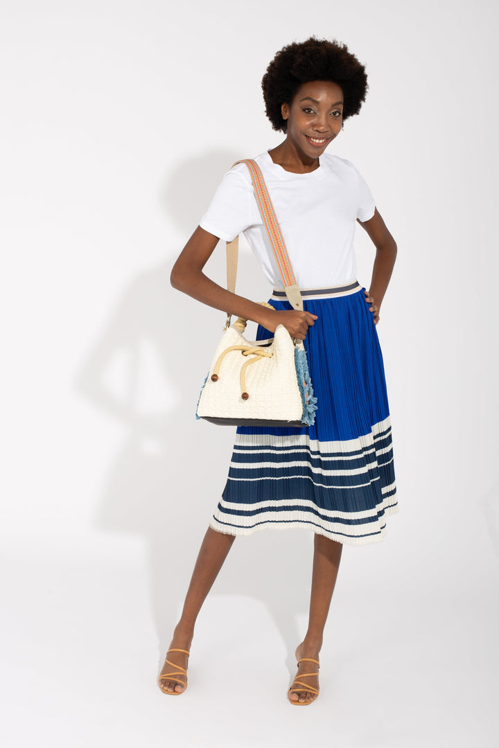 Woman in white shirt and blue skirt holding a white handbag