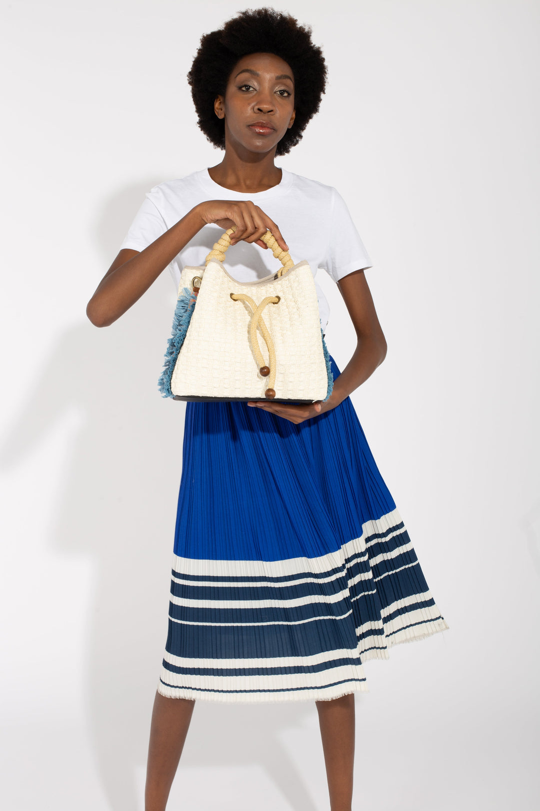 Fashionable woman holding a stylish white handbag with rope handles, wearing a blue and white striped skirt and white top