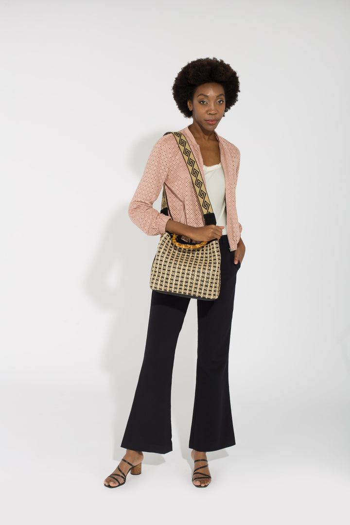 Woman in stylish attire with pink blazer, white top, black flared pants, and patterned shoulder bag, standing against white backdrop