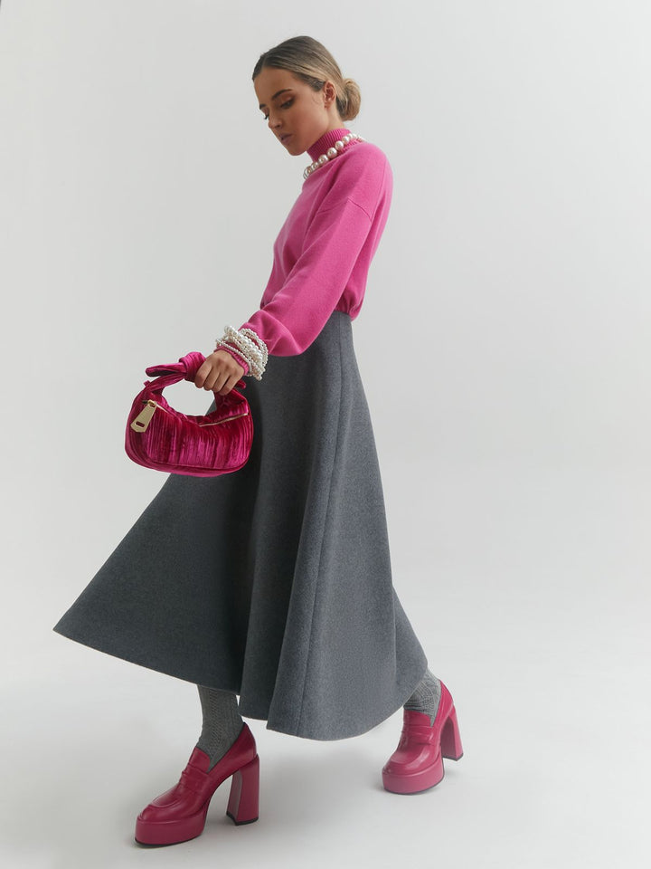 Woman wearing a pink sweater and gray skirt holds a red purse