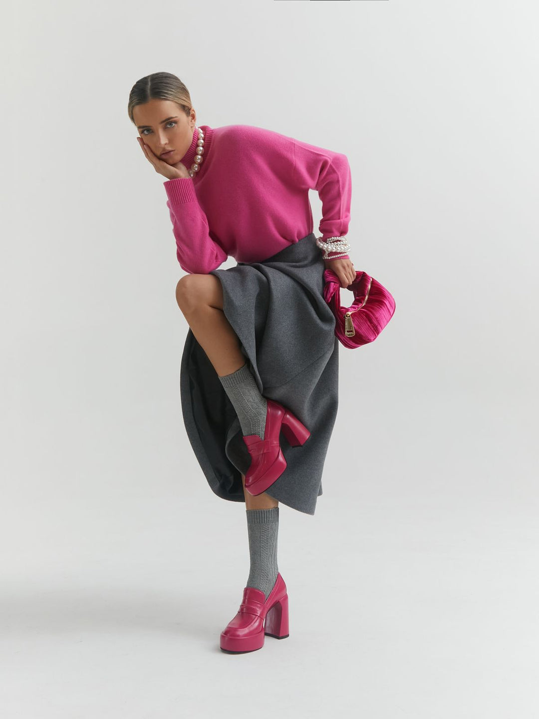 Woman in stylish outfit with pink sweater, gray skirt, and pink accessories posing confidently