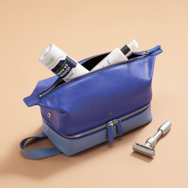 Blue toiletry bag with skincare products and razor on beige background