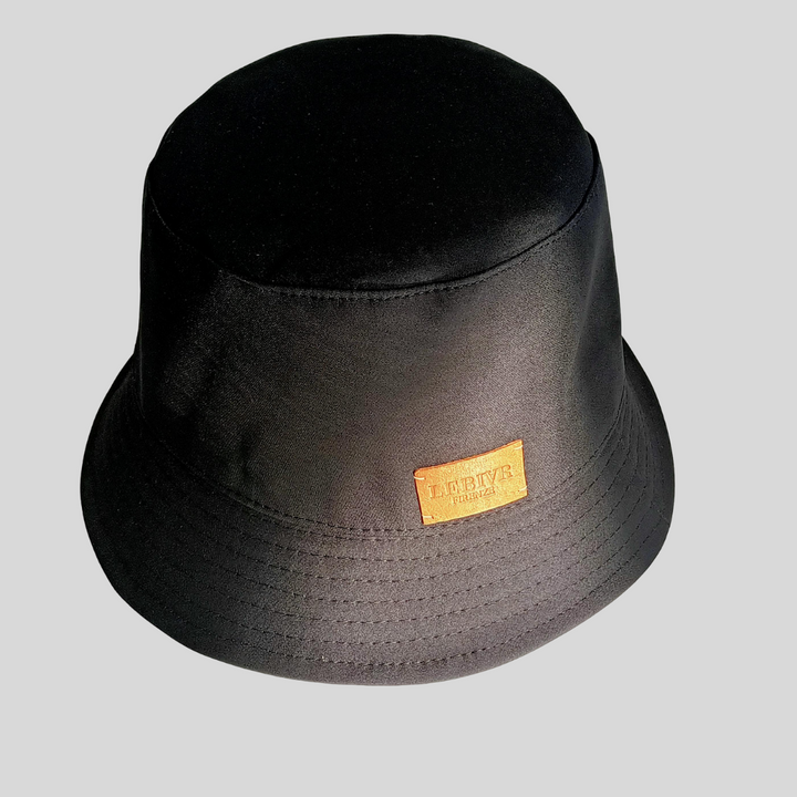 Black bucket hat with tan leather logo patch on gray background