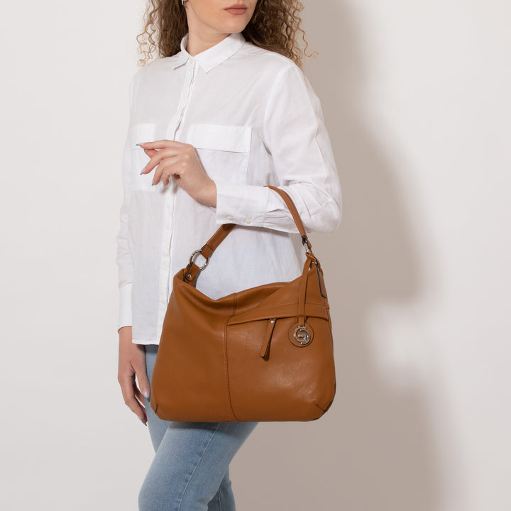 Woman holding a stylish brown leather handbag wearing a white blouse and blue jeans