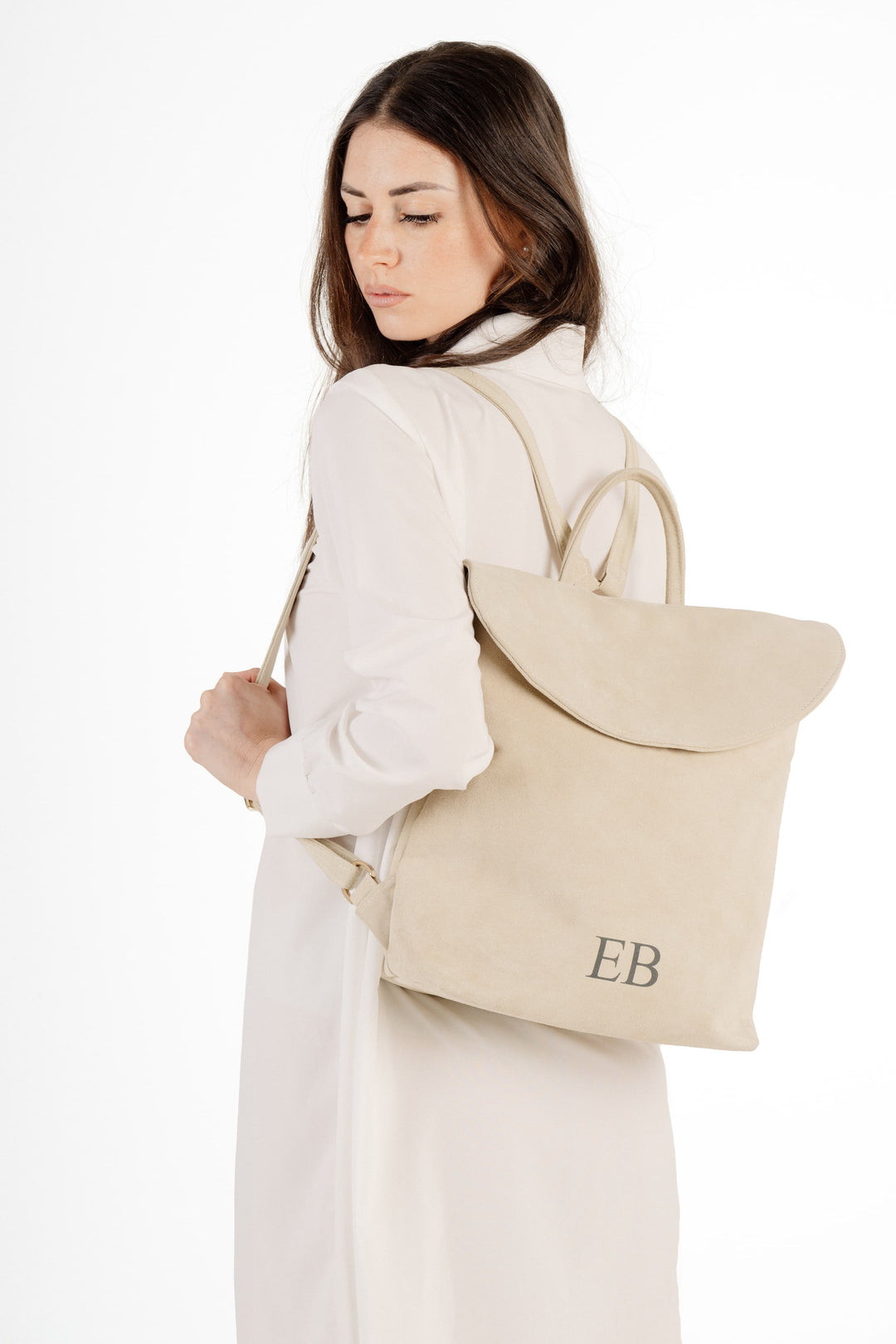 Woman wearing a white dress carrying a beige backpack with EB initials