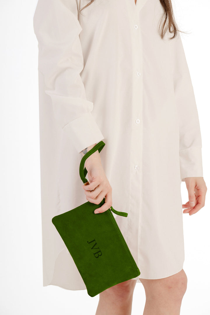 Person holding green suede clutch bag while wearing white button-up shirt dress