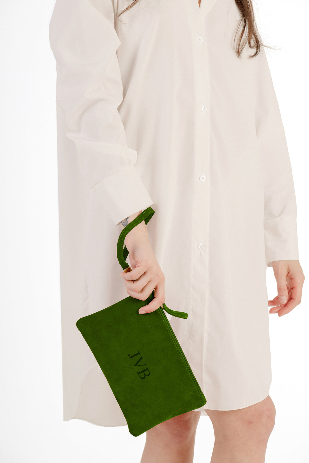Woman holding a green monogrammed clutch bag wearing a white shirt dress