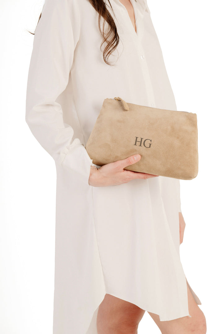 Woman in white shirt dress holding beige suede clutch with monogram initials HG