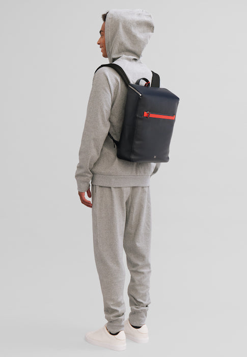 Person wearing gray tracksuit and hoodie with a navy backpack featuring a red zipper