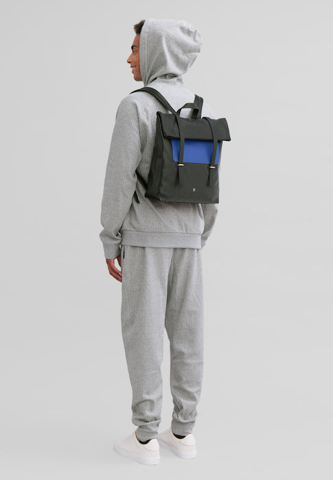 Man in grey tracksuit and hoodie wearing black and blue backpack