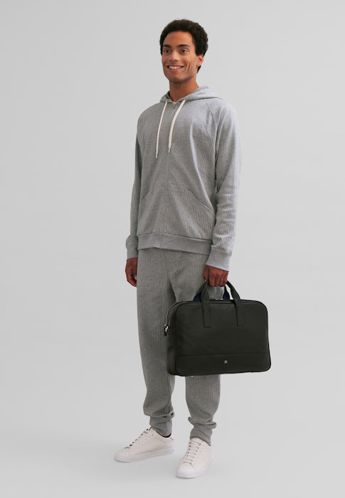 Man in gray loungewear holding black travel bag against a plain background